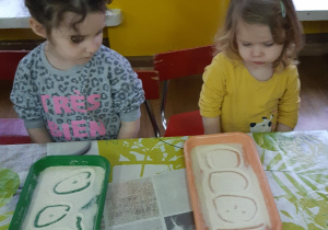 dwie dziewczynki rysują w kaszy