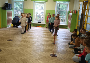 dzieci stoją w dwóch rzędach przed pachołkami ustawionymi na holu