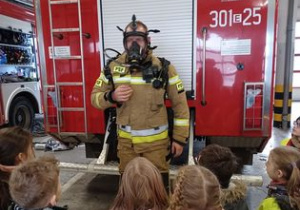 strażak prezentuje dzieciom specjalnie ubranie używane do akcji gaśniczych