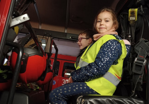 dziewczynka i chłopiec siedzą w wozie strażackim