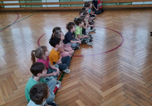 dzieci siedza w linii na sali gimnastycznej