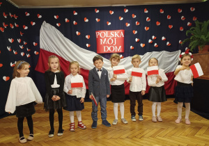 dzieci ubrane na galowo trzymają flagi