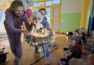 aktorzy niosą lalkę w podświetlonym gnieździe