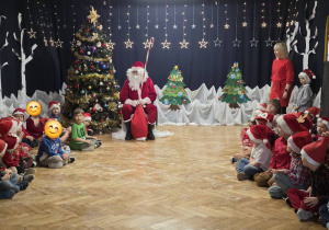 w centralnej części holu siedzi Mikołaj po jego prawej i lewej stronie siedzą dzieci