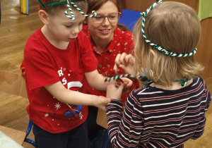 dziewczynka i chłopiec trzymają w rękach kolorowe, plecione ozdoby przypominające świąteczne wianuszki lub opaski.