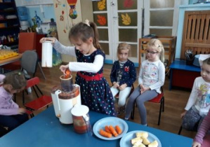 dziewczynka wkłada marchewke do sokowirówki